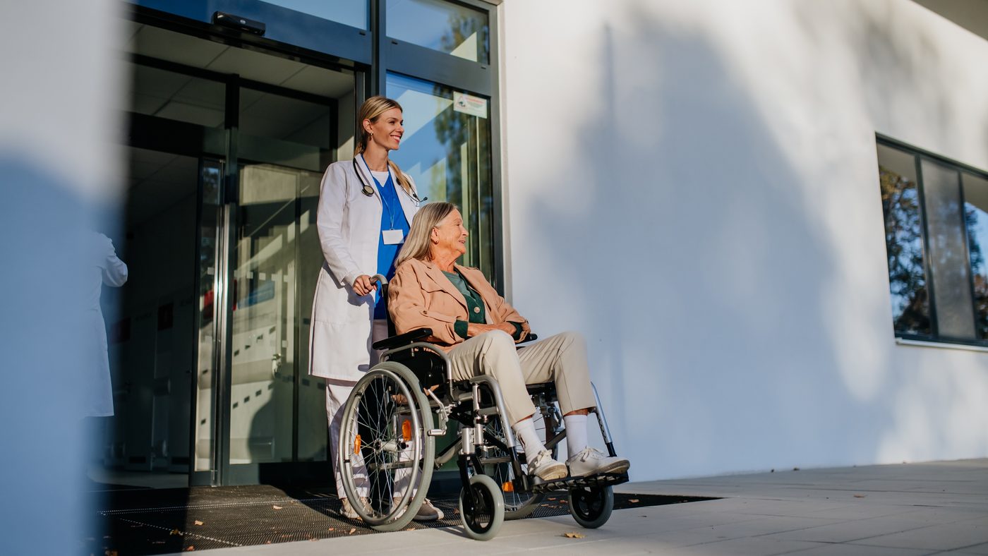 Doctora acompaña a una paciente adulta mayor en silla de ruedas a la salida del hospital